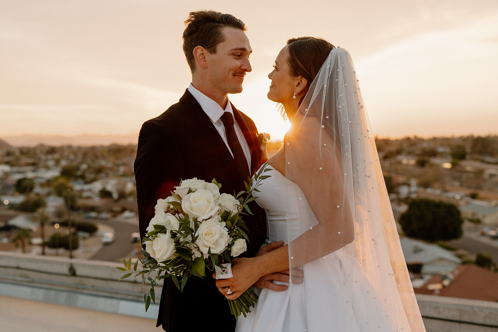 bride and groom looking at one another while holding bouquet at sunset