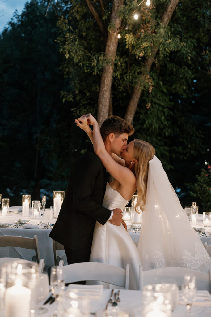 bride and groom kissing under twinkling lights at evening reception