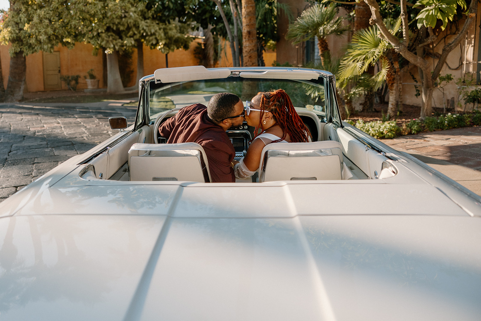 couple share a kiss in a vintage car during their engagement photos at the royal palms resort