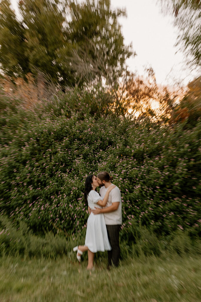 beautiful couple share a kiss in front of a flower wall during their engagement photos
