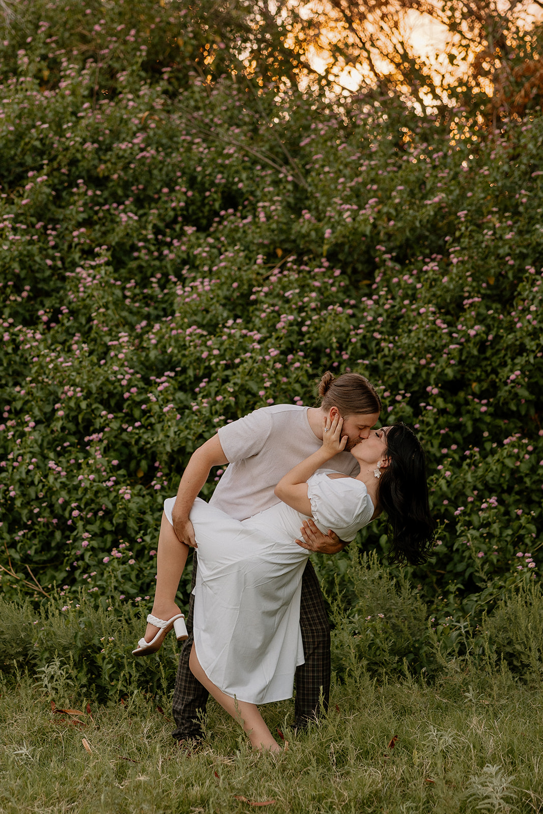 beautiful couple share a kiss in front of a flower wall during their engagement photos