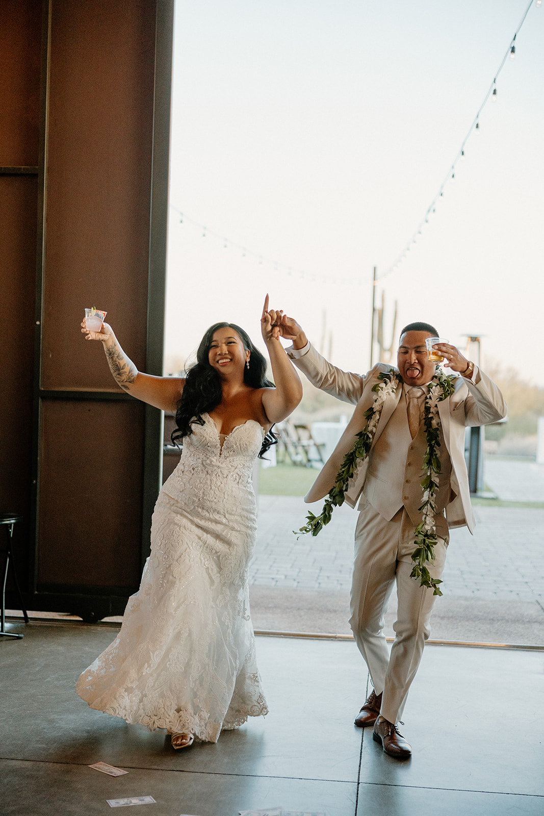 A joyful couple makes their grand entrance into their Arizona wedding reception, holding hands and smiling wide.

