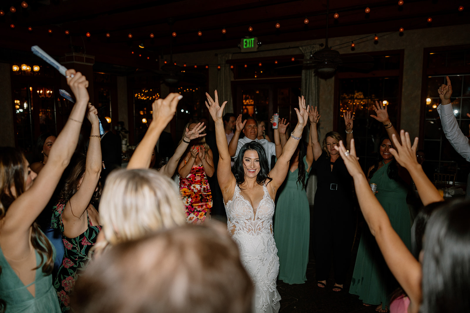 The bride leads a group dance with hands in the air, surrounded by guests hyping her up on the dance floor at an Arizona wedding reception.

