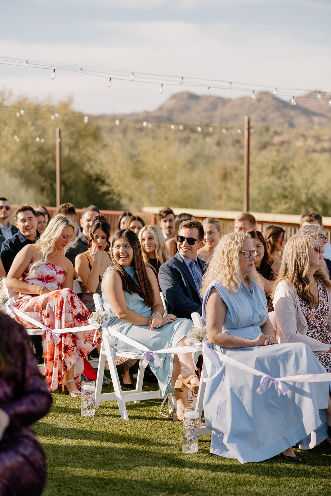 Wedding guests seated and smiling during a sunny outdoor ceremony at The Cove at Bartlett Lake wedding venue.

