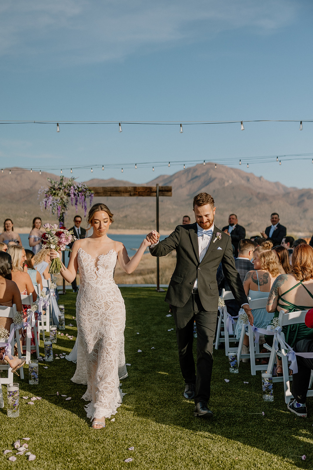 Bride and groom walking up the aisle, surrounded by guests, mountains, and a glistening lake view—an unforgettable day at a waterfront wedding venue in Arizona.