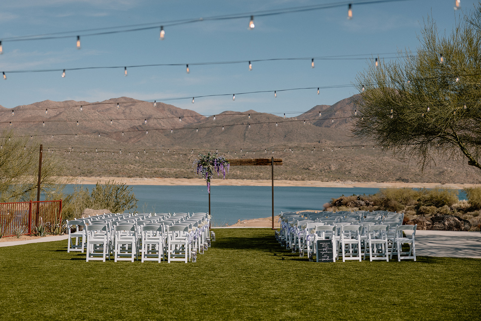 Outdoor ceremony setup overlooking the water with white chairs, string lights, and a floral arch at The Cove at Bartlett Lake