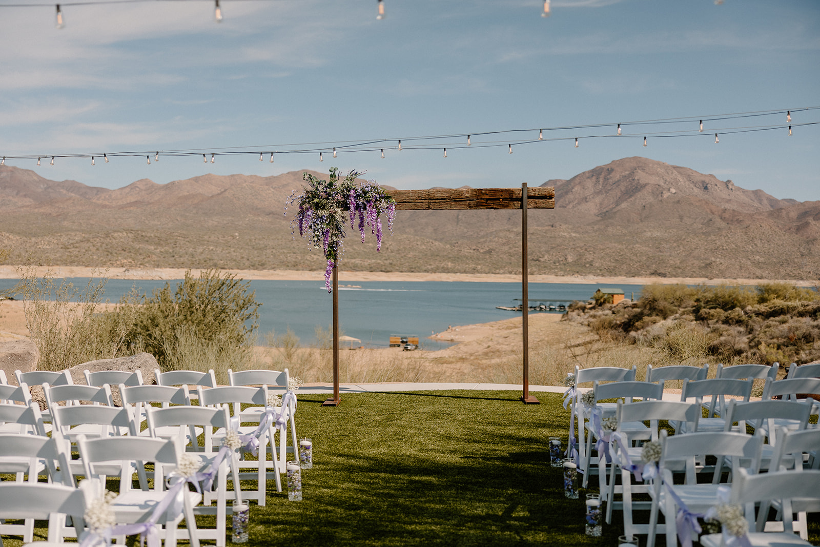 A wide view of a waterfront ceremony setup with white chairs, delicate lavender accents, and a floral-draped wooden arch—all perfectly styled at one of the most breathtaking waterfront wedding venues in Arizona.