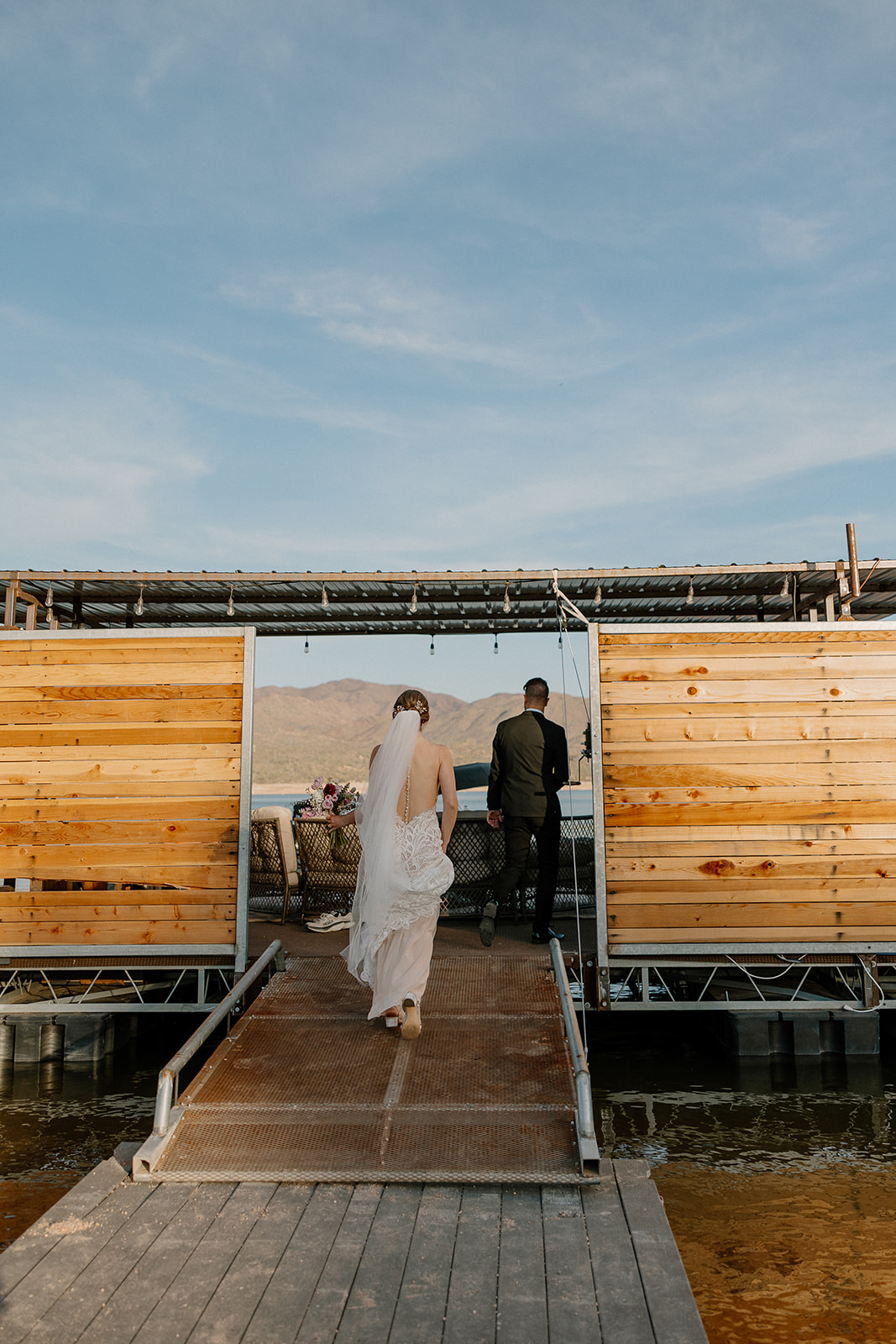 Bride and groom walk hand-in-hand down the dock toward their boat at The Cove at Bartlett Lake wedding venue.