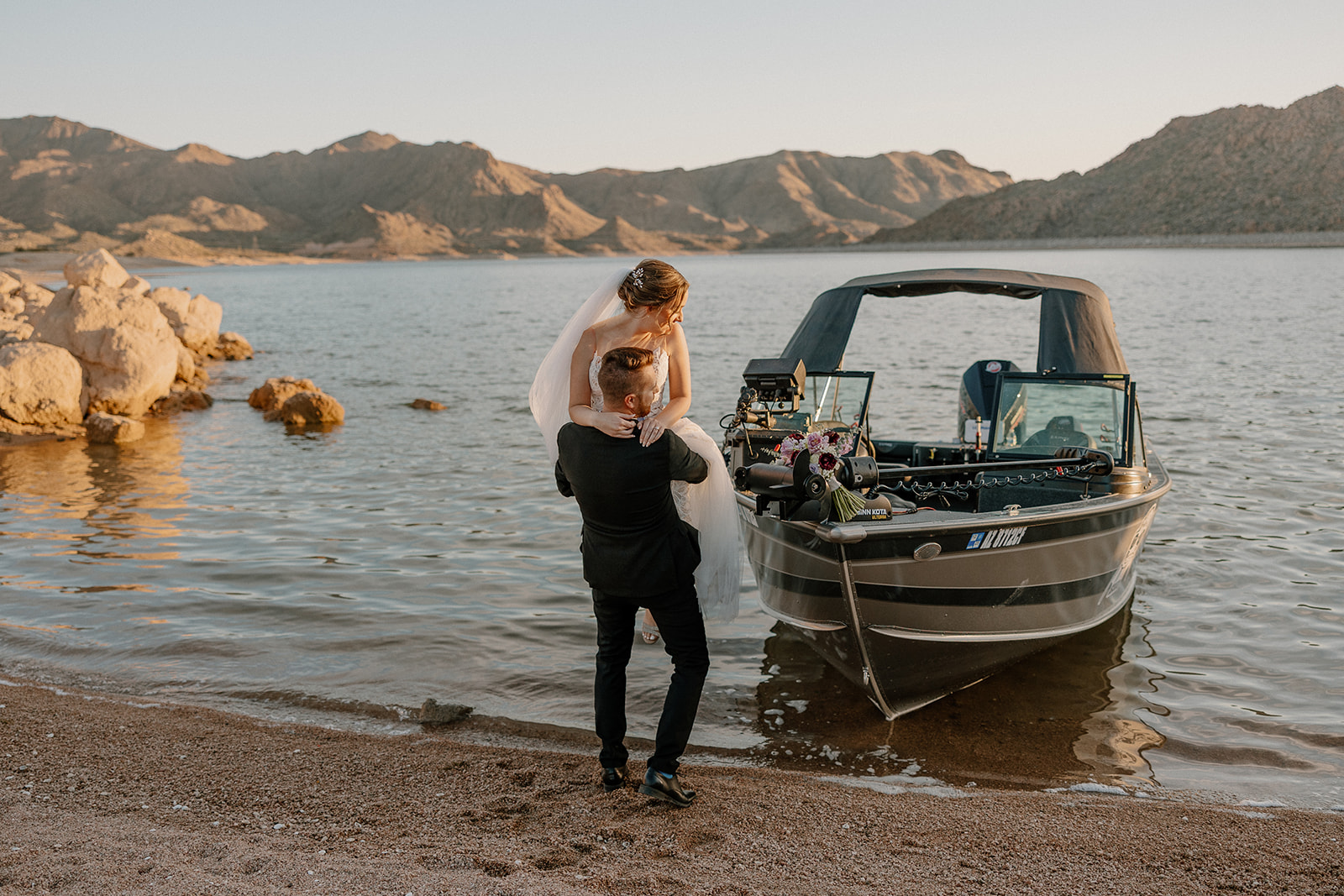 A groom lifts his bride at the edge of a lake next to a decorated boat, perfectly blending adventure with love at one of the most scenic waterfront wedding venues in Arizona.