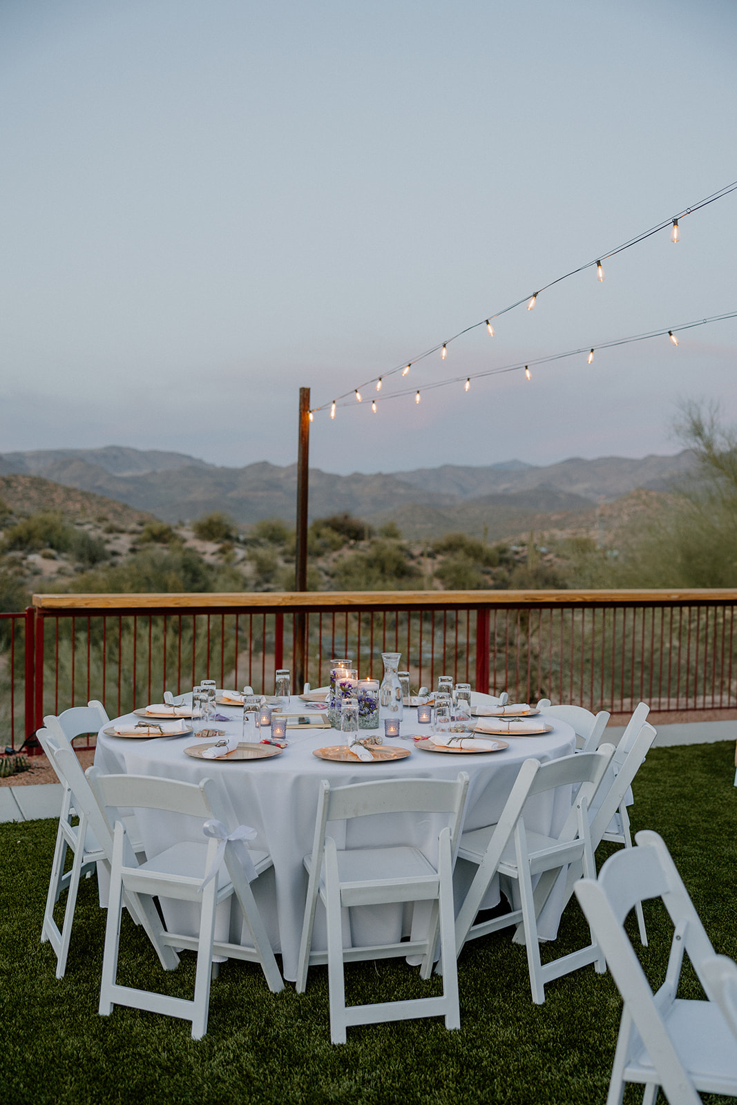 Outdoor reception table with white chairs and string lights against desert mountain backdrop at The Cove at Bartlett Lake wedding.


