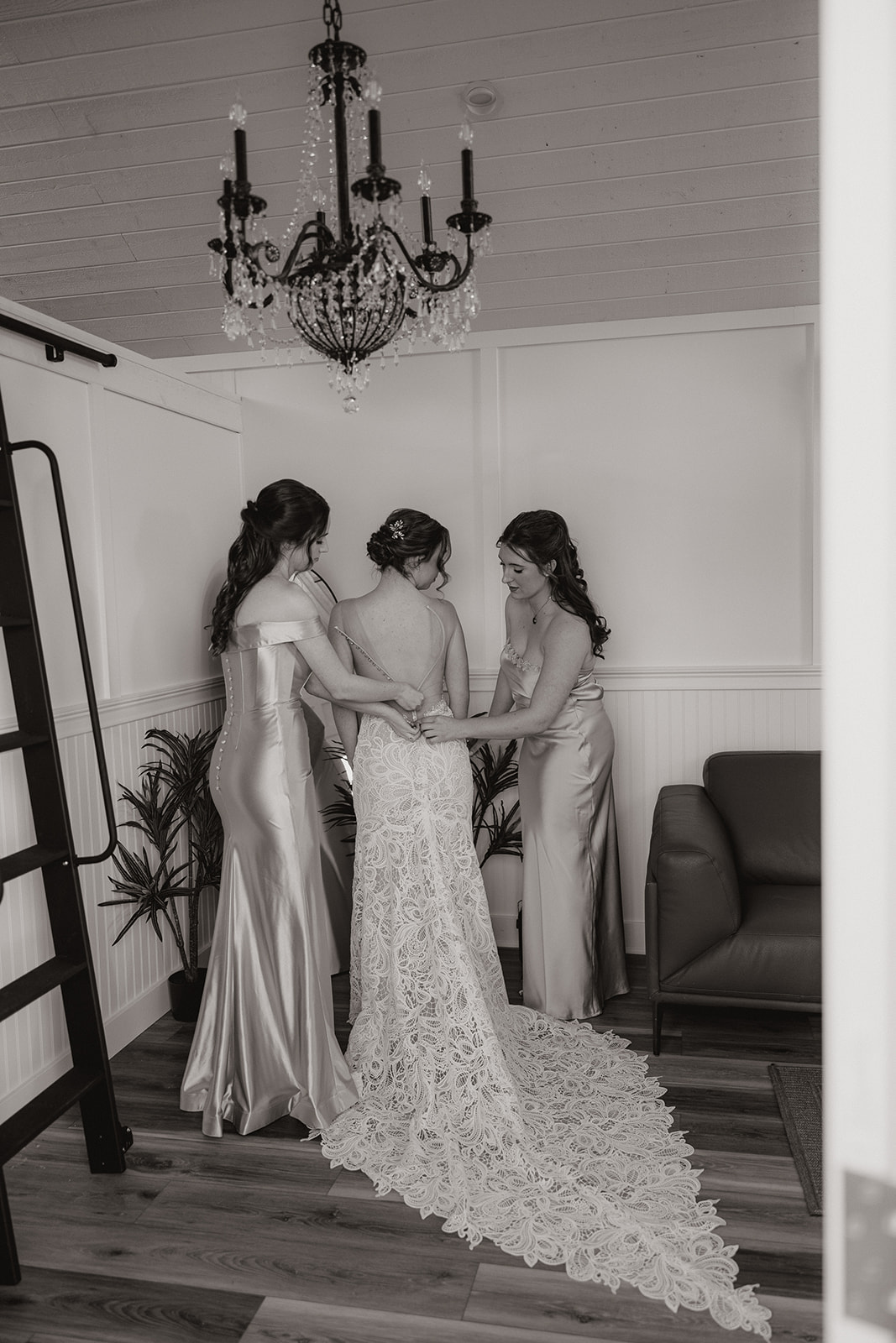Bride getting zipped into her lace gown by bridesmaids in a bridal suite at The Cove at Bartlett Lake wedding venue.

