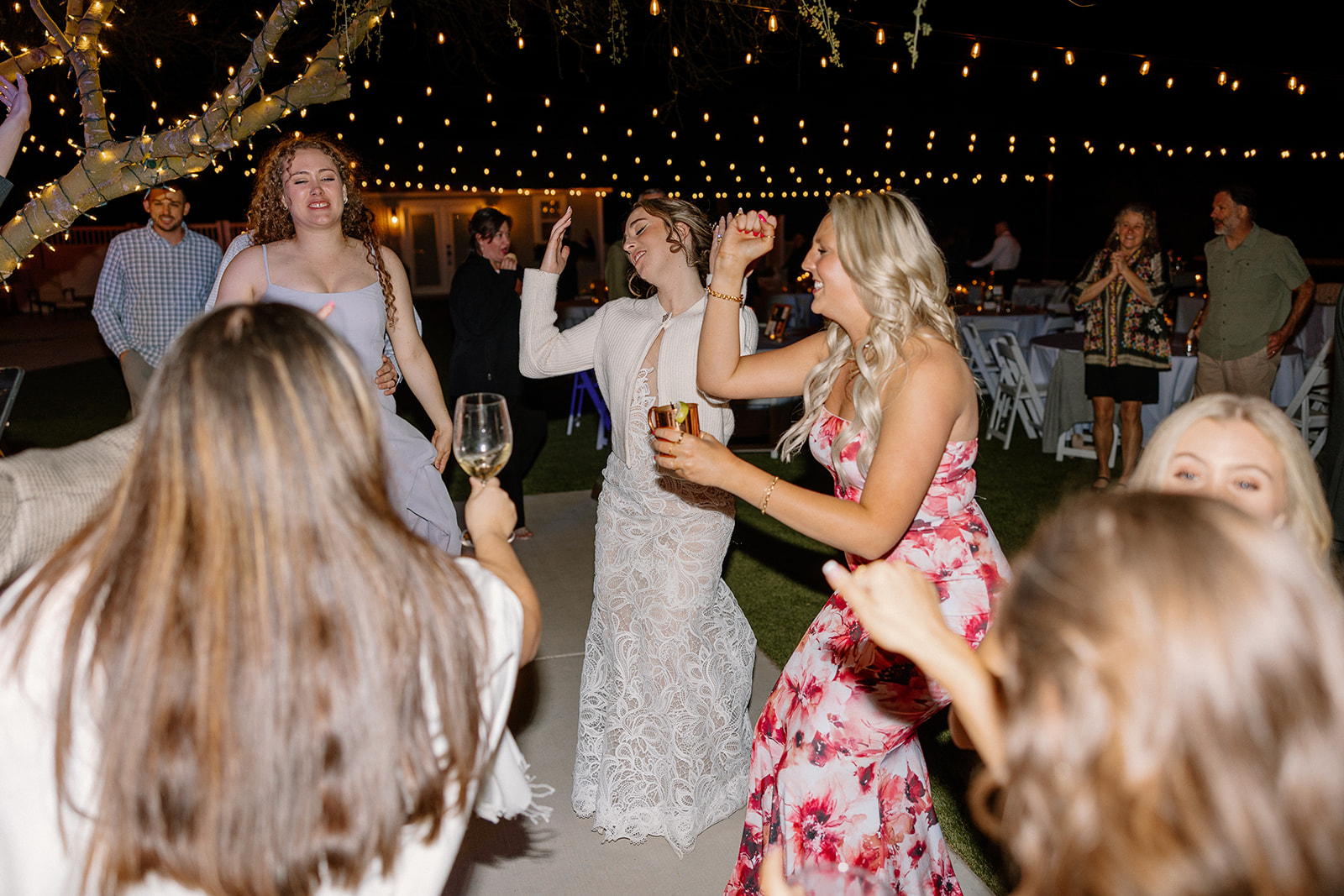 Bride surrounded by friends and bridesmaids on the dance floor under string lights at The Cove at Bartlett Lake wedding reception.


