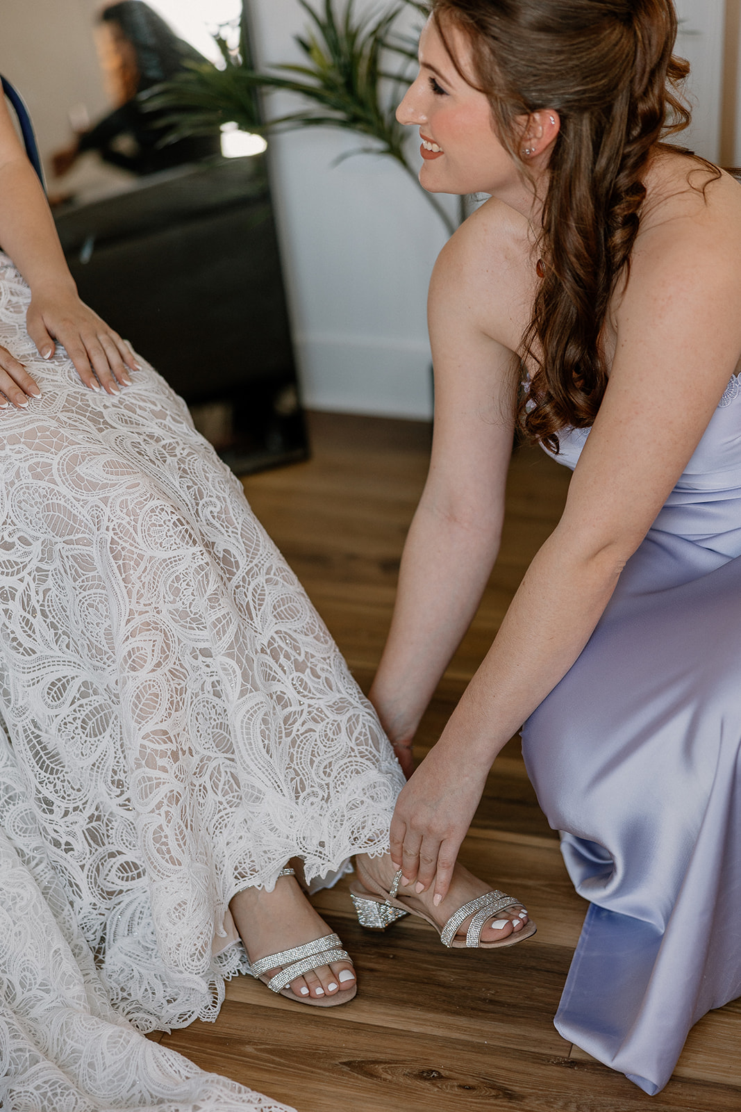 Bridesmaid in lavender dress helping the bride with sparkly heels on wedding day at The Cove at Bartlett Lake.


