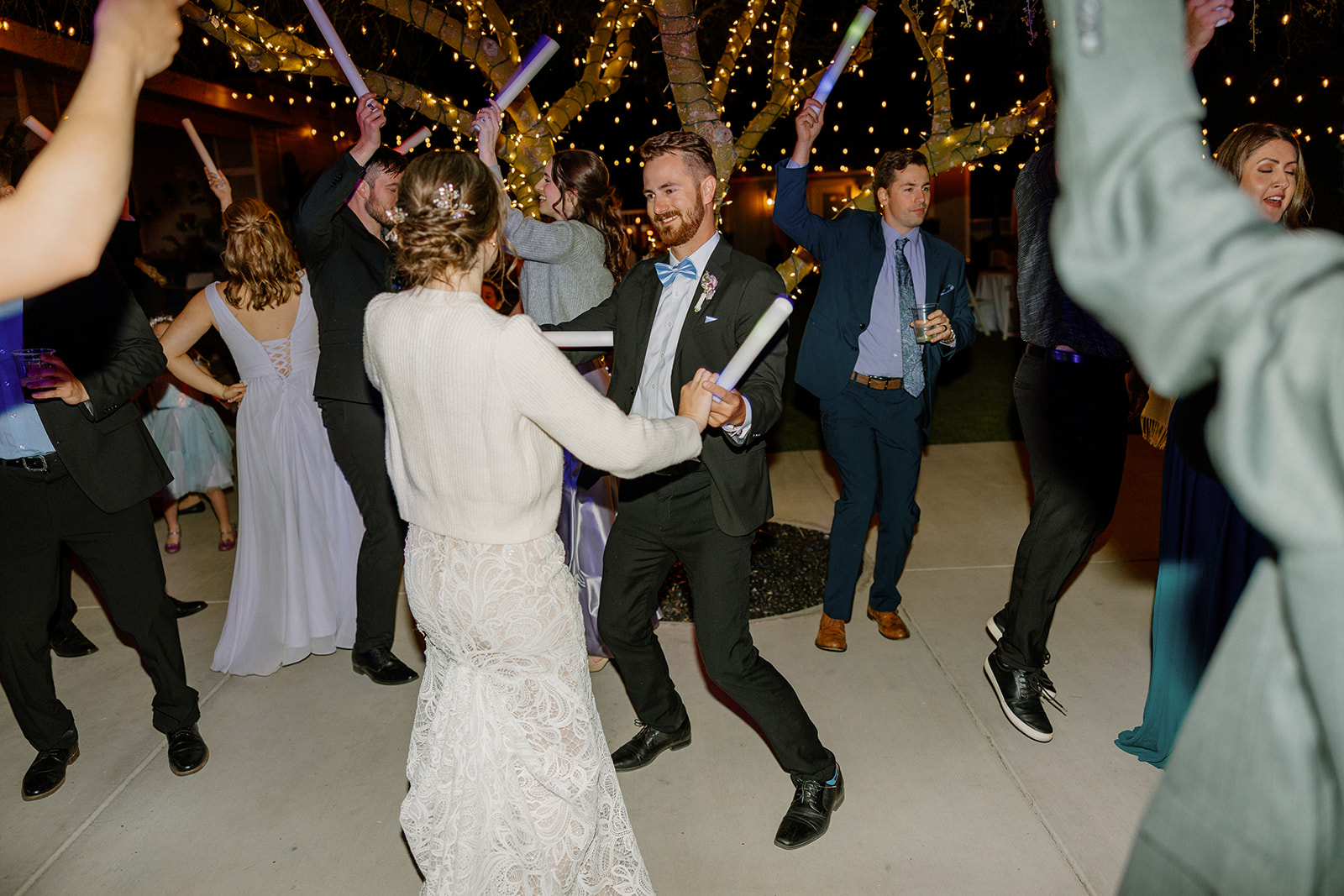 Dance floor moment under string lights as the couple parties with guests, glow sticks in hand.