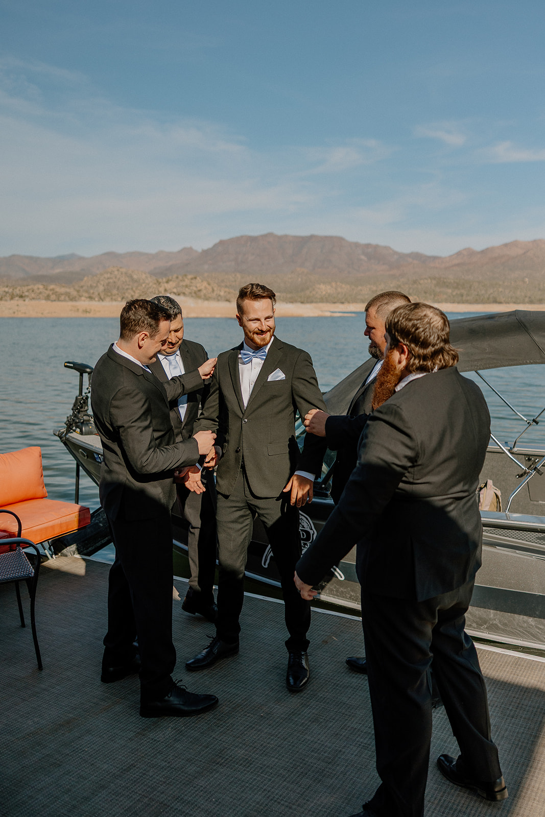 Groom getting ready with groomsmen on the dock at The Cove at Bartlett Lake wedding, with the lake and boat in the background.

