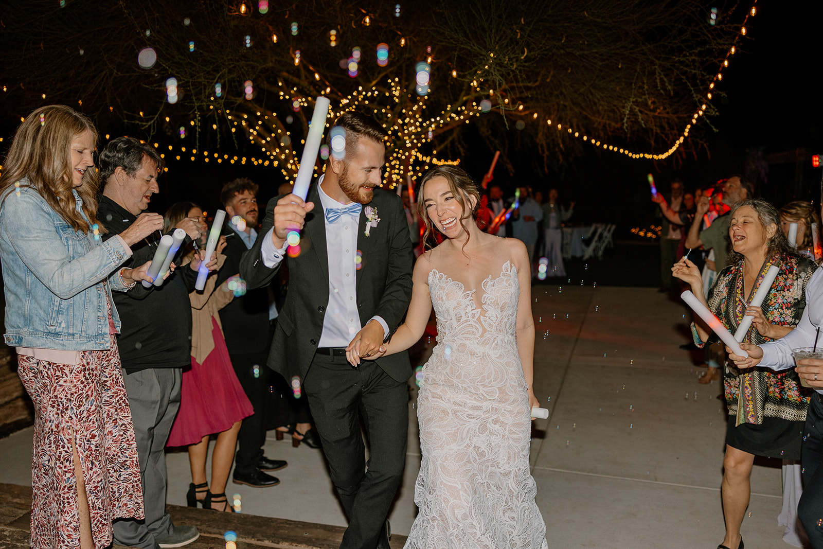 Bride and groom walking through a glowing bubble send-off with LED wands at The Cove at Bartlett Lake wedding celebration.

