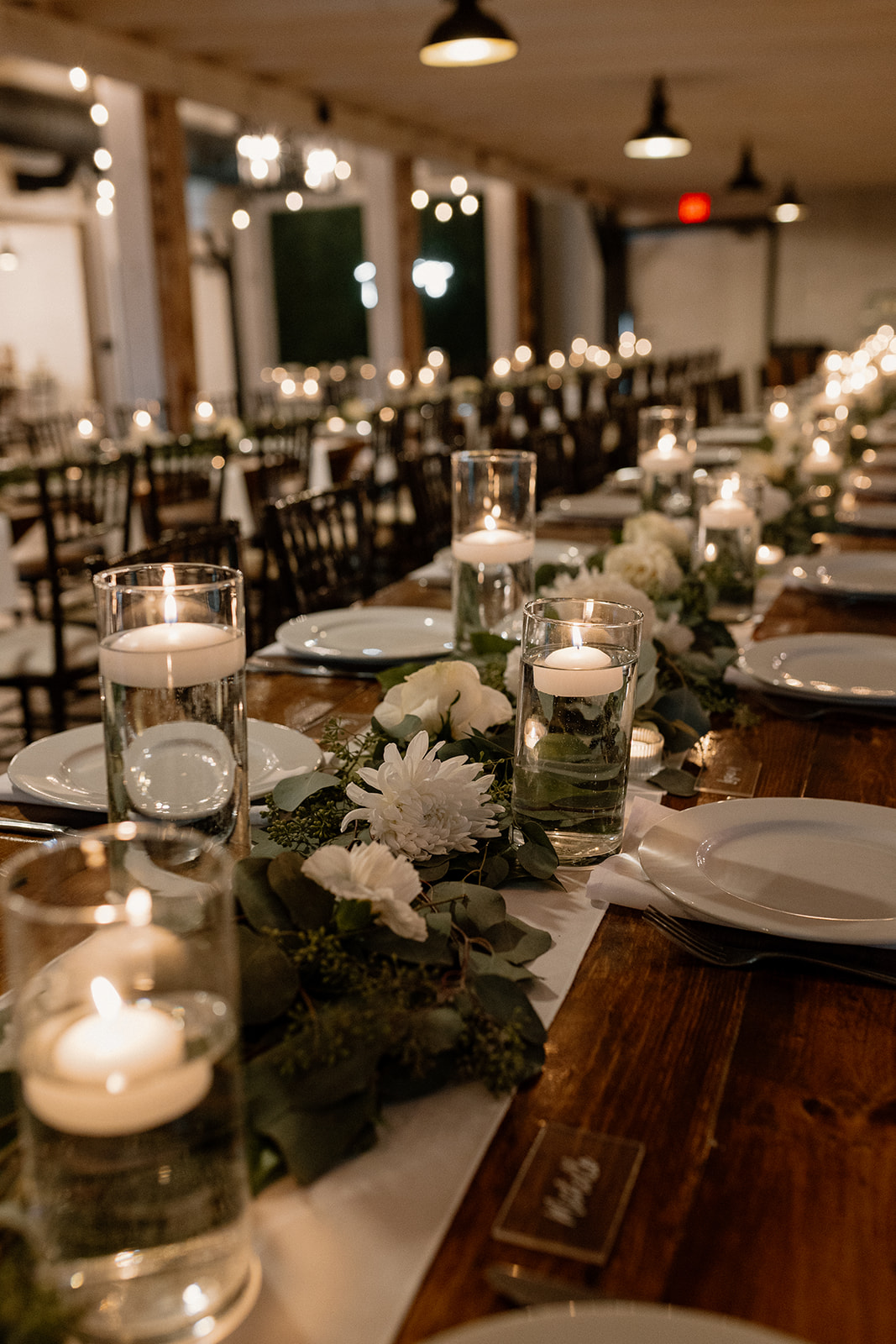 A candlelit indoor reception table with elegant floating candles and white floral garlands, creating a romantic, cozy ambiance.