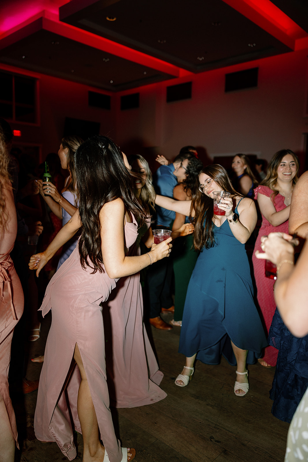 Guests dance under red neon lights, letting loose on the floor during a lively indoor Arizona wedding reception.