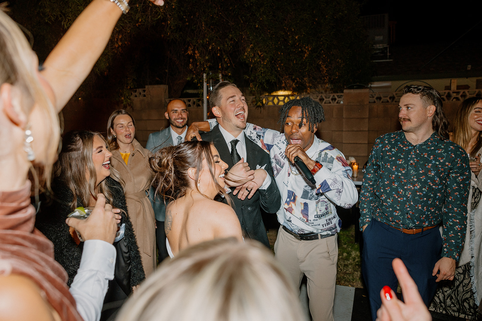 Guests sing along with a hype man on the mic during a fun, interactive dance floor moment at a wedding reception.