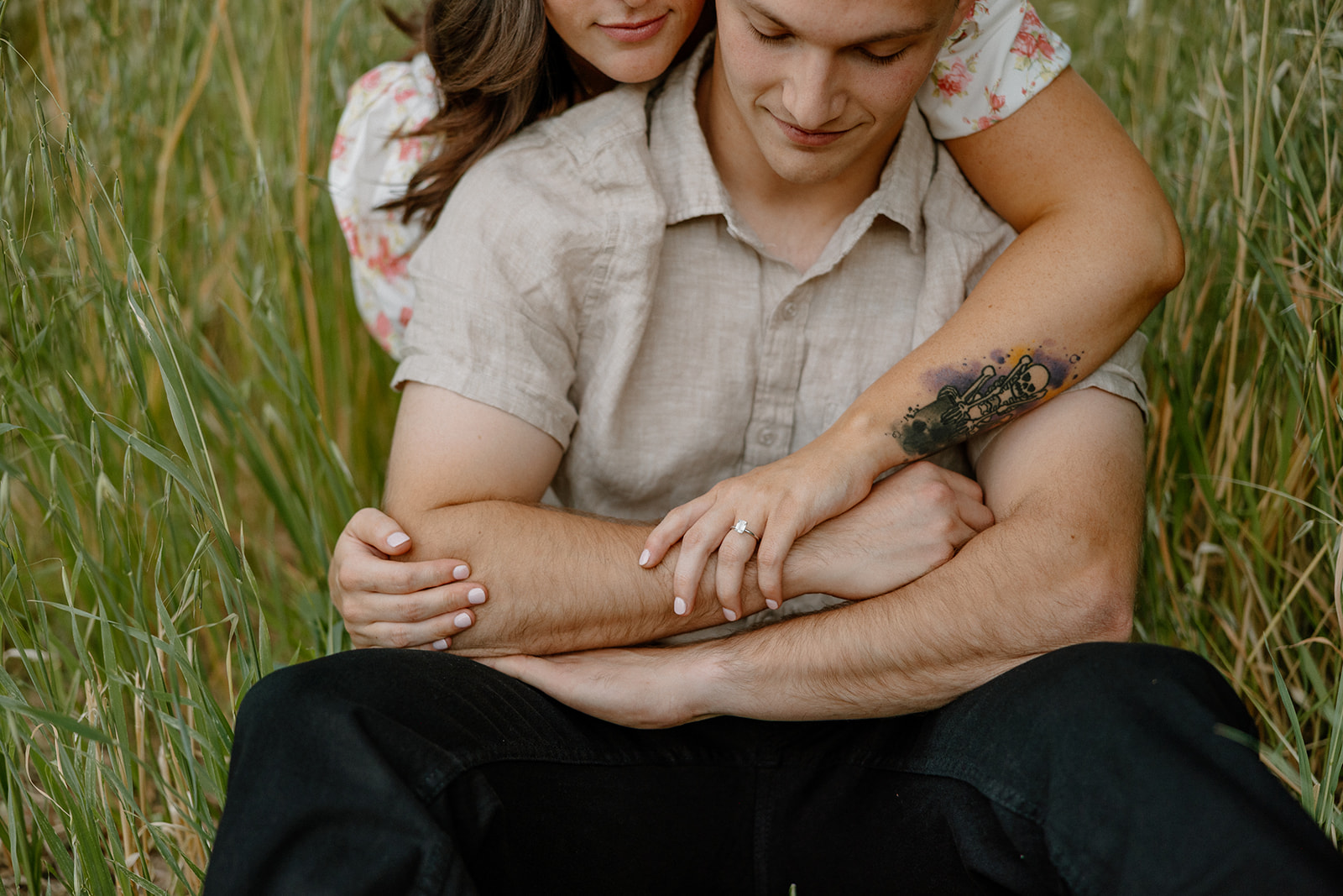 Man and woman sitting on together in green grass during orchard engagement photos in Arizona