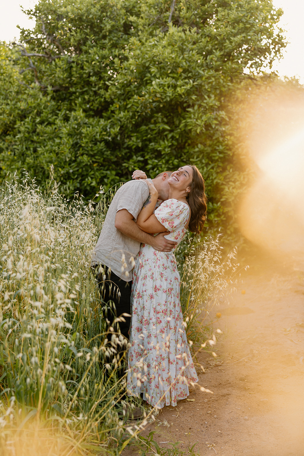 Man making fiance laugh by tickling her neck during golden hour engagement photos