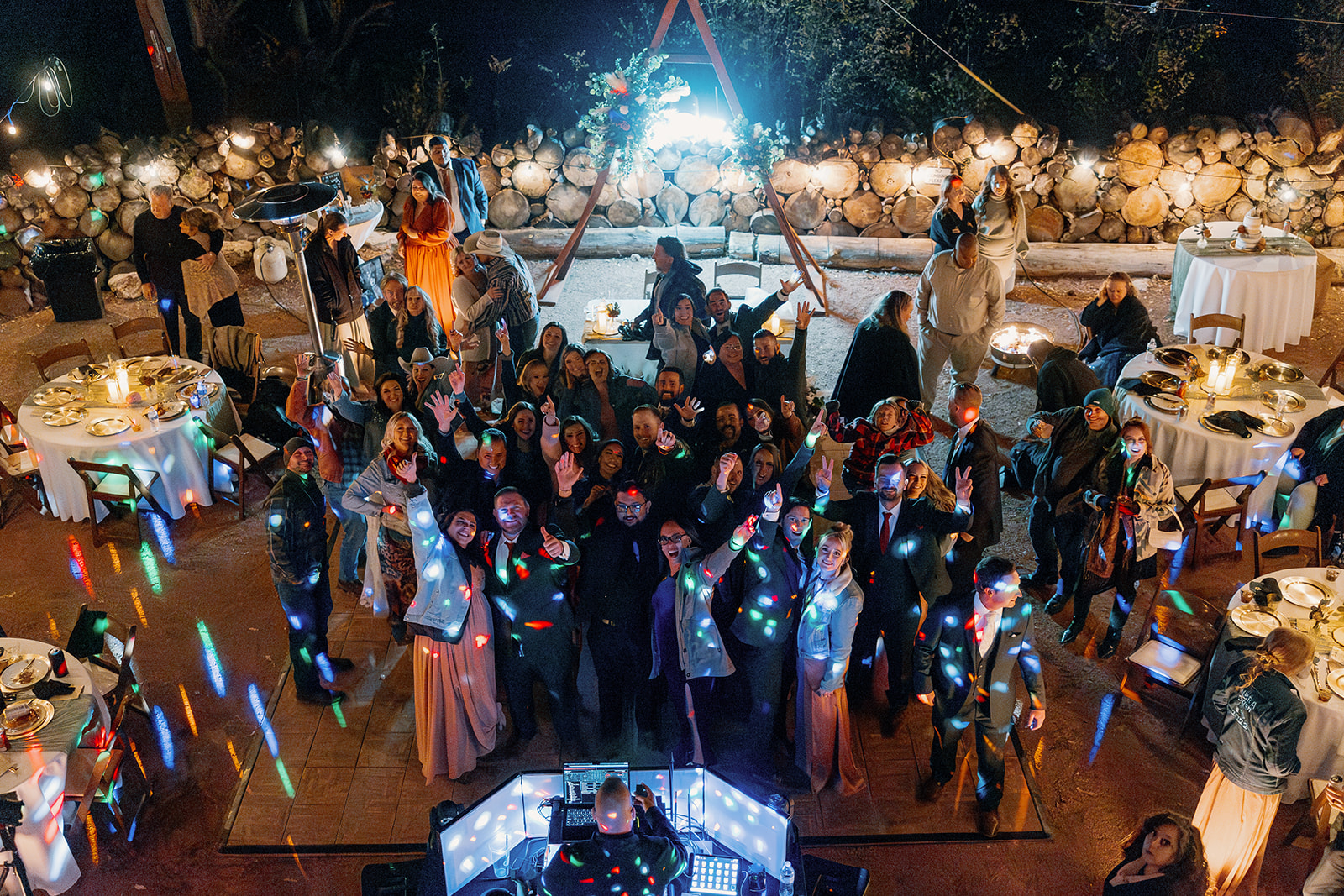 A lively crowd surrounds the DJ booth under string lights at an outdoor Arizona wedding reception, everyone dancing and cheering for the camera.