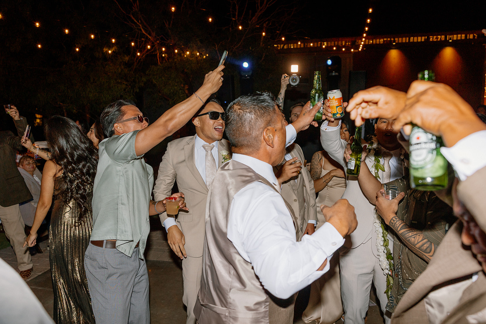 Groomsmen and guests cheer with beers and cocktails raised high during an outdoor Arizona wedding reception dance party.

