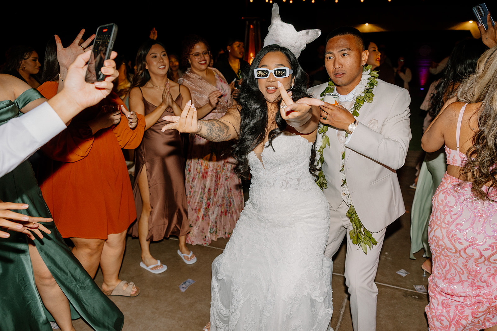 The bride rocks fun sunglasses and throws double peace signs as she dances with guests at her bold and lively wedding reception.