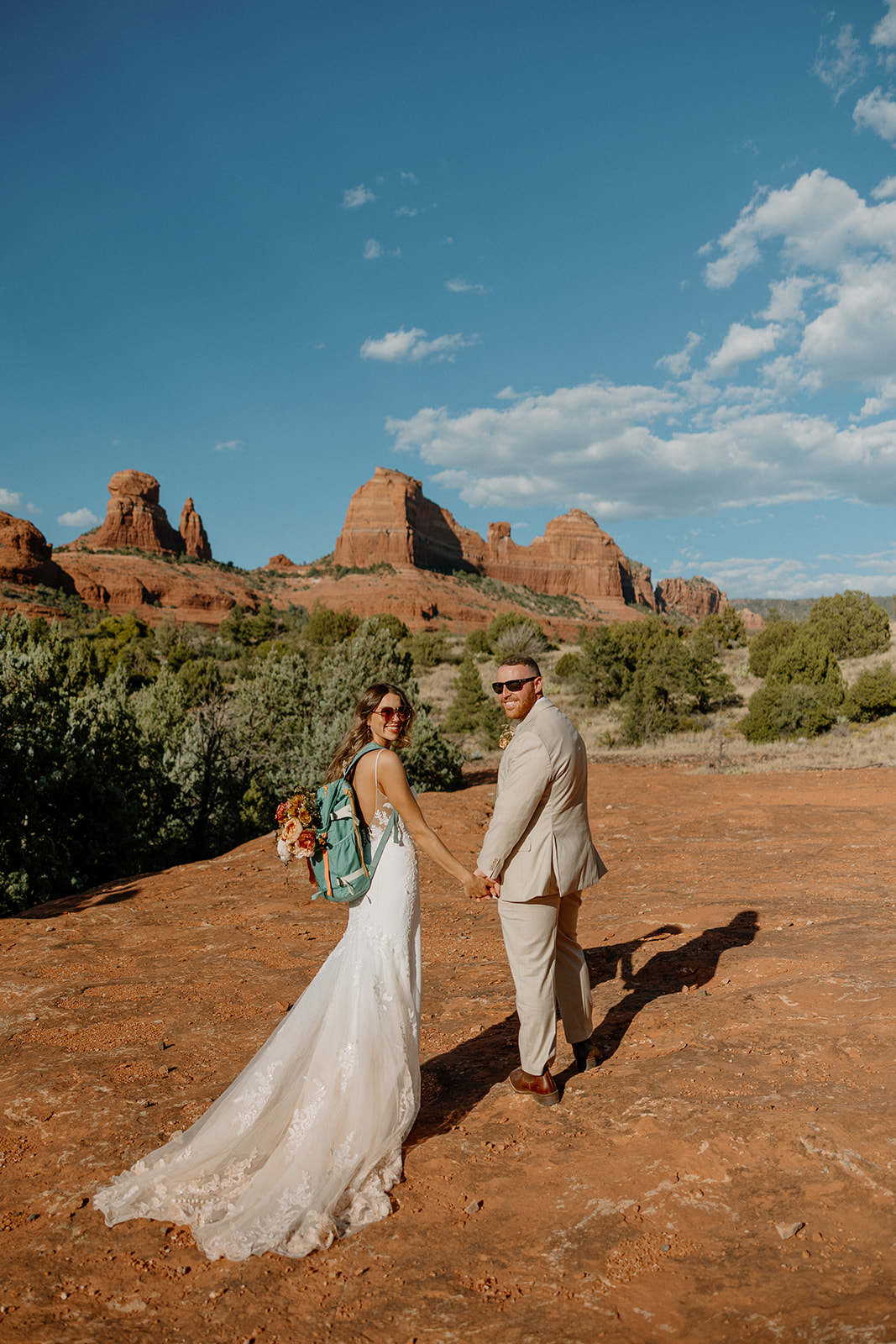 Bride wearing backpack and holding hands with her groom before going on wedding day hike