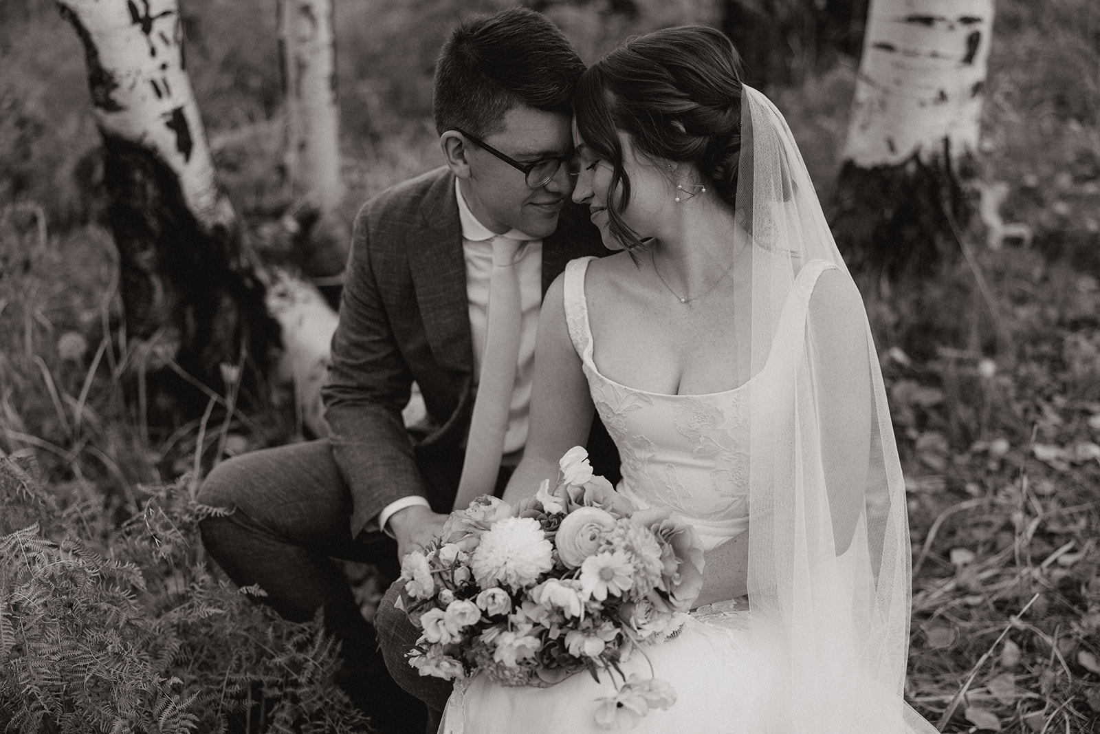 Intimate black and white portrait of a bride and groom resting together beneath the aspens, soft light filtering in.