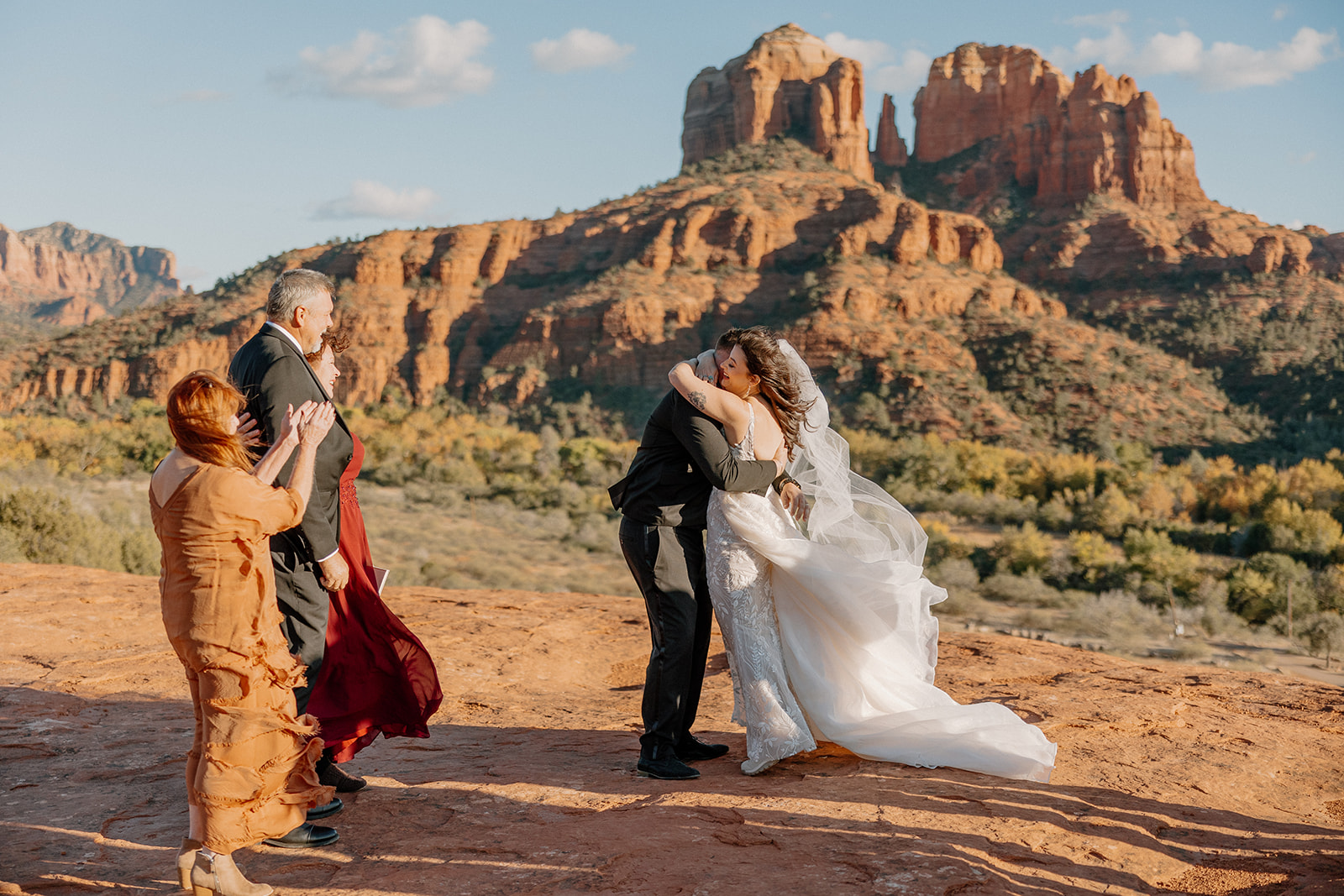 Newlyweds hugging joyfully on the red rocks of Sedona, surrounded by cheering guests at their Arizona elopement.