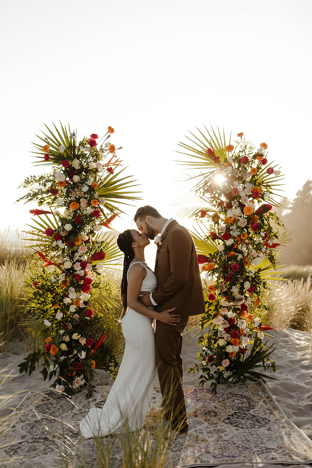 Bride and groom sharing a kiss beneath a tropical floral altar during their stylish elopement ceremony.