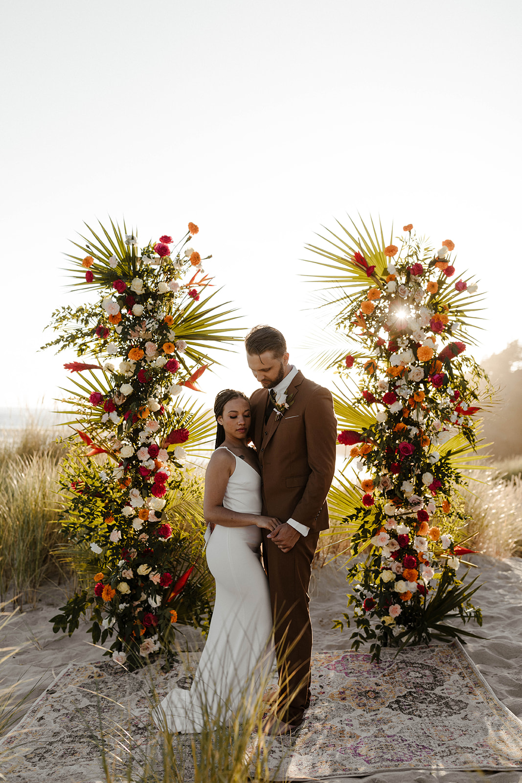Couple standing in a soft embrace under a colorful tropical altar during their modern elopement.