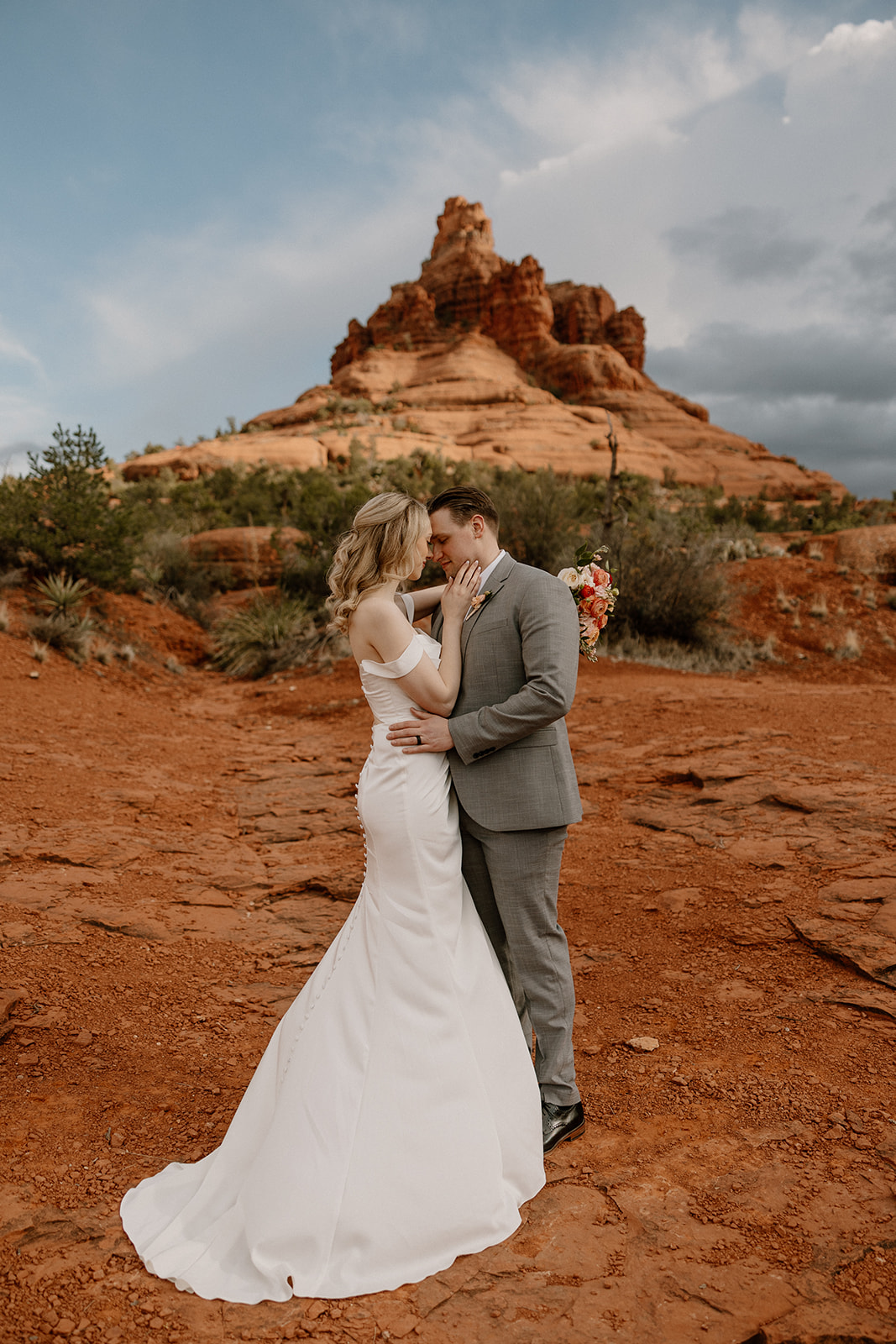 Intimate moment in front of Bell Rock, with bride and groom in elegant wedding attire under a dramatic sky