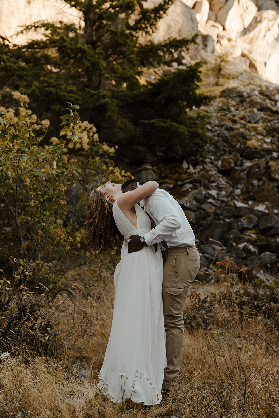 Bride leaning back laughing in the arms of her partner in a rugged mountain setting, all carefree energy and love.
