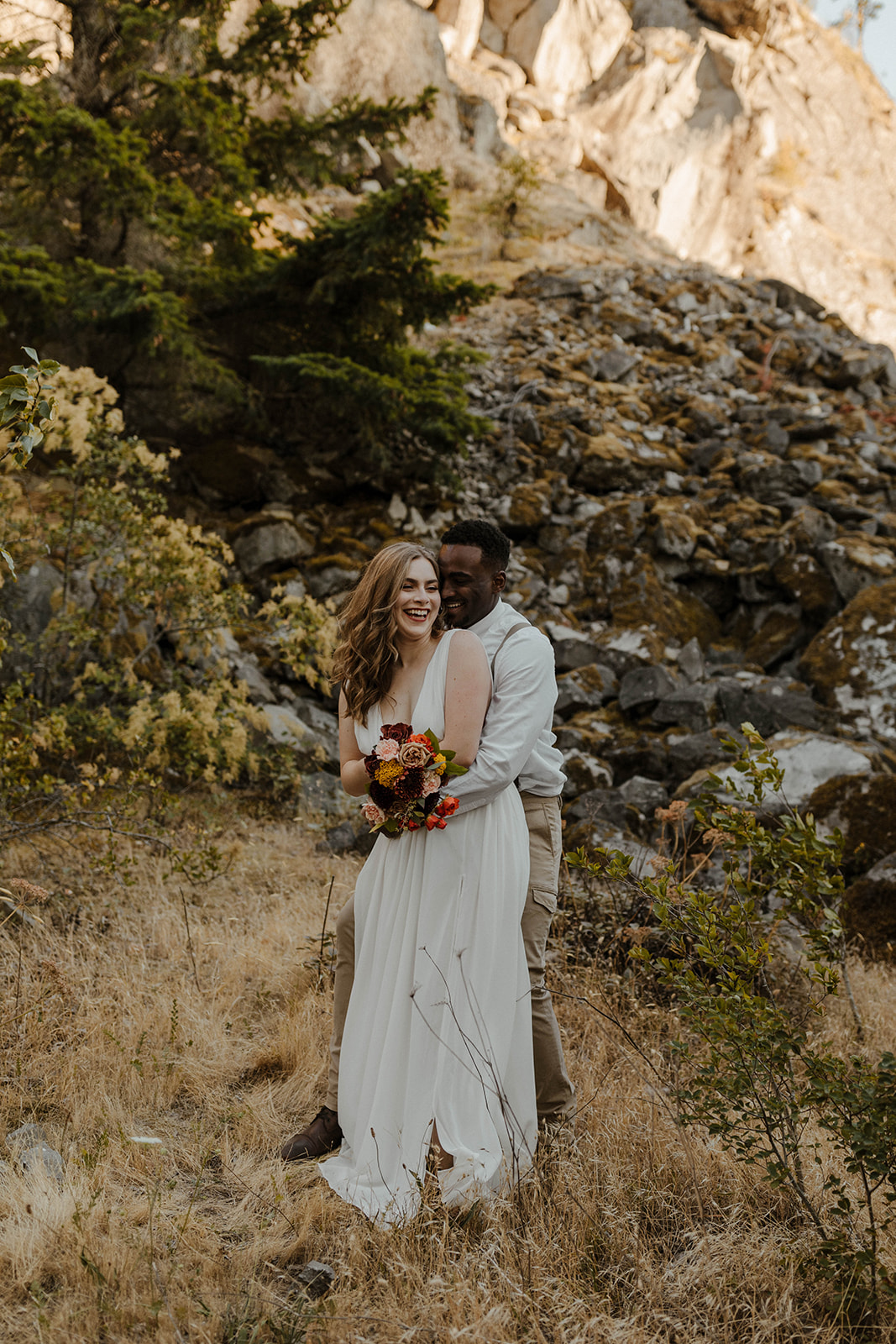 Bride and groom sharing a joyful embrace in front of a rugged mountain backdrop, celebrating their intimate elopement.
