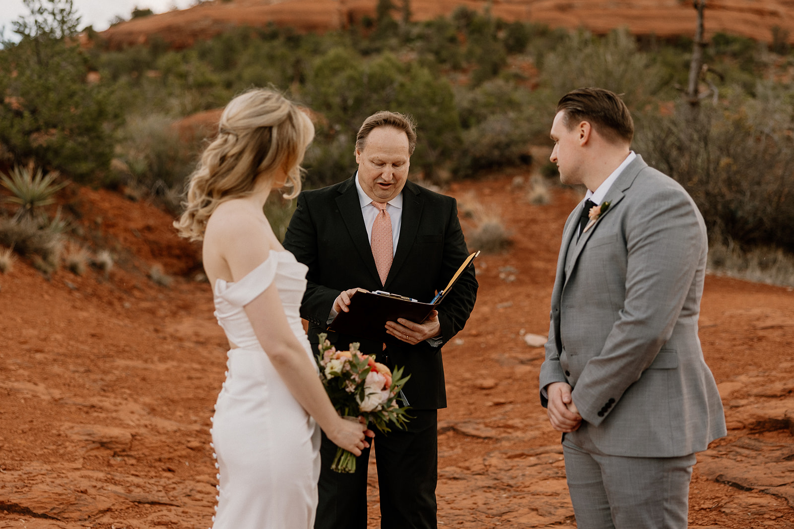 Bride and groom standing with their officiant on red rock terrain in Sedona, mid-ceremony after deciding how to tell your family you're eloping.
