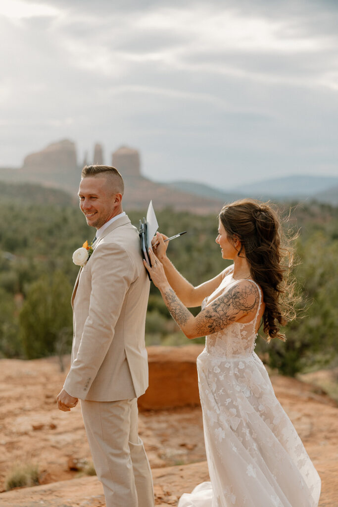 Bride writing her vows on the groom’s back with Cathedral Rock in the distance—one of many creative ways couples embrace the moment after figuring out how to tell your family you're eloping.
