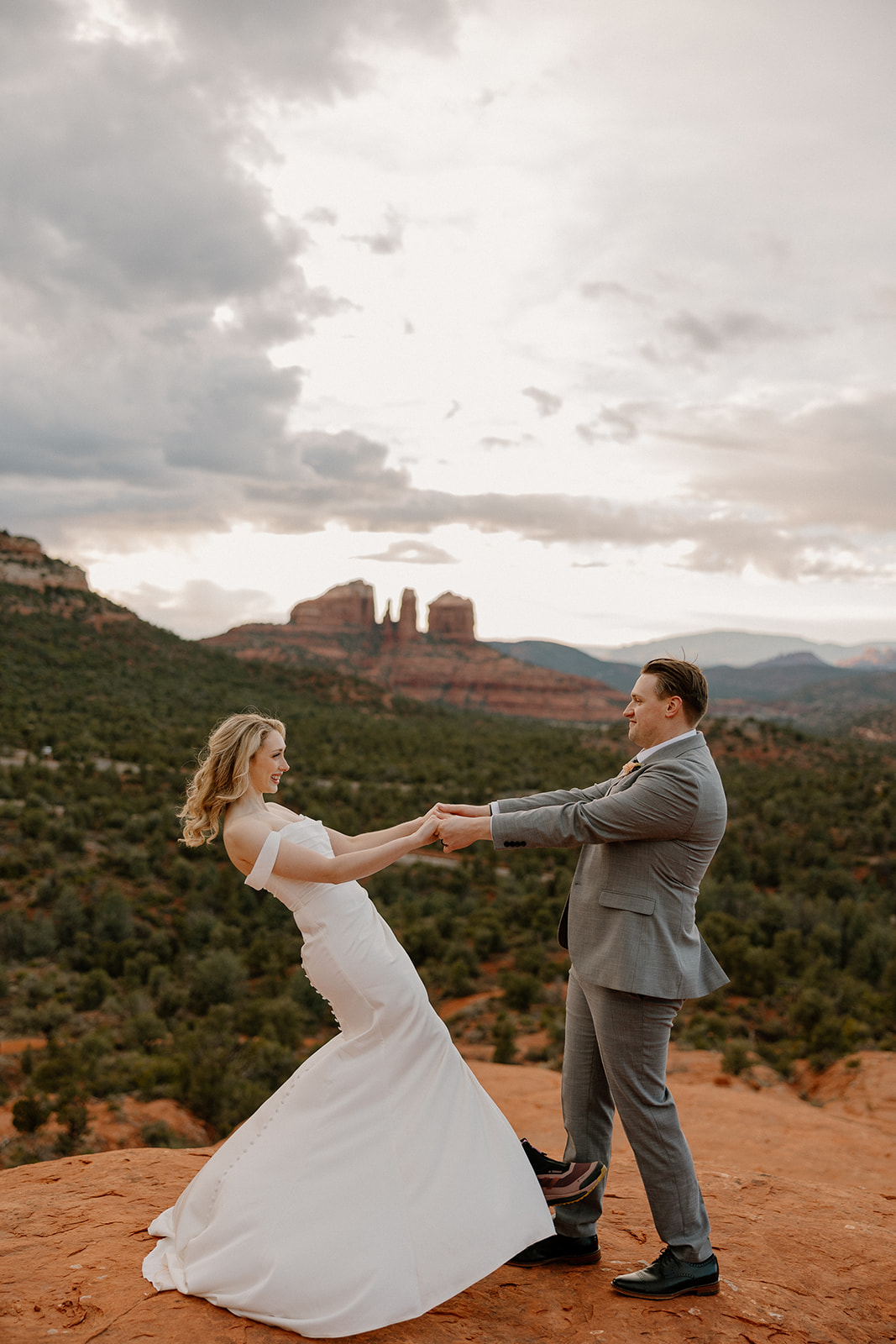 Bride and groom laughing while pulling each other’s hands on a Sedona cliff, Cathedral Rock glowing in the distance—showing the joy that comes after figuring out how to tell your family you're eloping.
