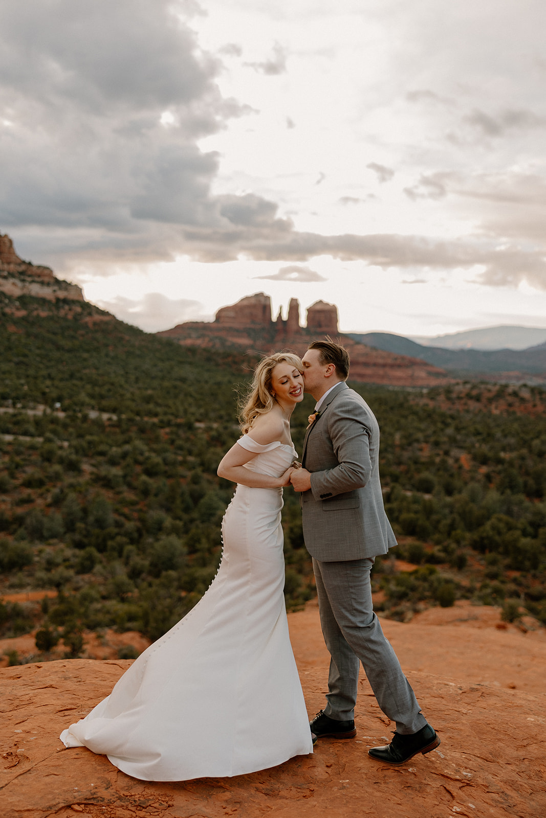 Bride and groom holding hands and laughing on Sedona’s red rock cliffs, celebrating love after navigating how to tell your family you're eloping.
