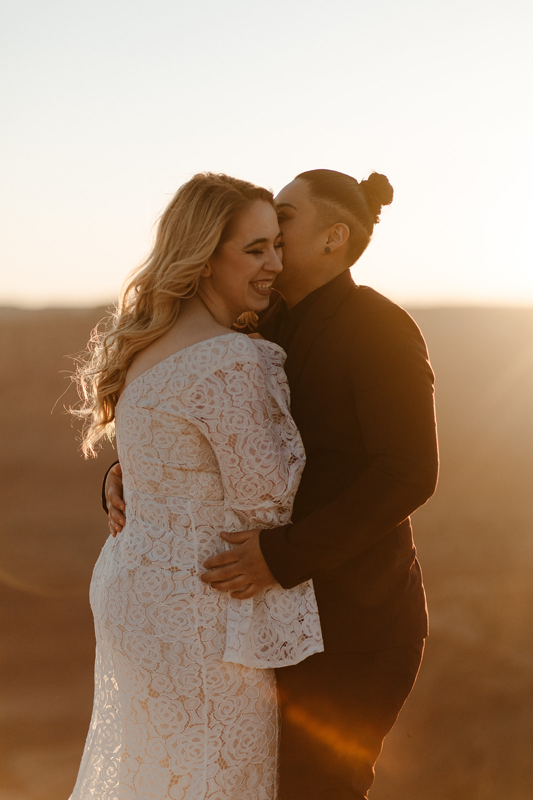 Golden-hour portrait of two brides laughing and embracing at the canyon’s edge, glowing with happiness after they figured out how to tell their family they're eloping.