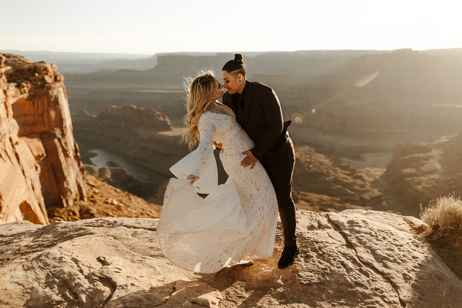 Cliffside elopement featuring groom wedding attire in a rich maroon suit, twirling his bride in the golden canyon breeze at Dead Horse Point.