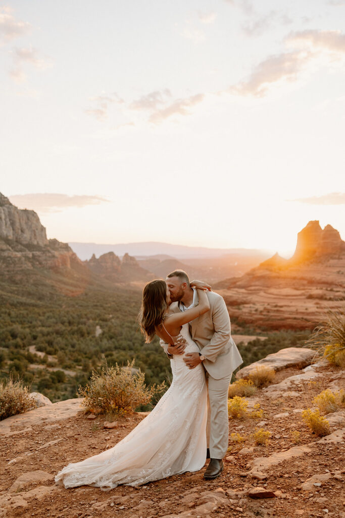 Couple kissing at golden hour on Sedona cliffs, bride in backless lace wedding attire

