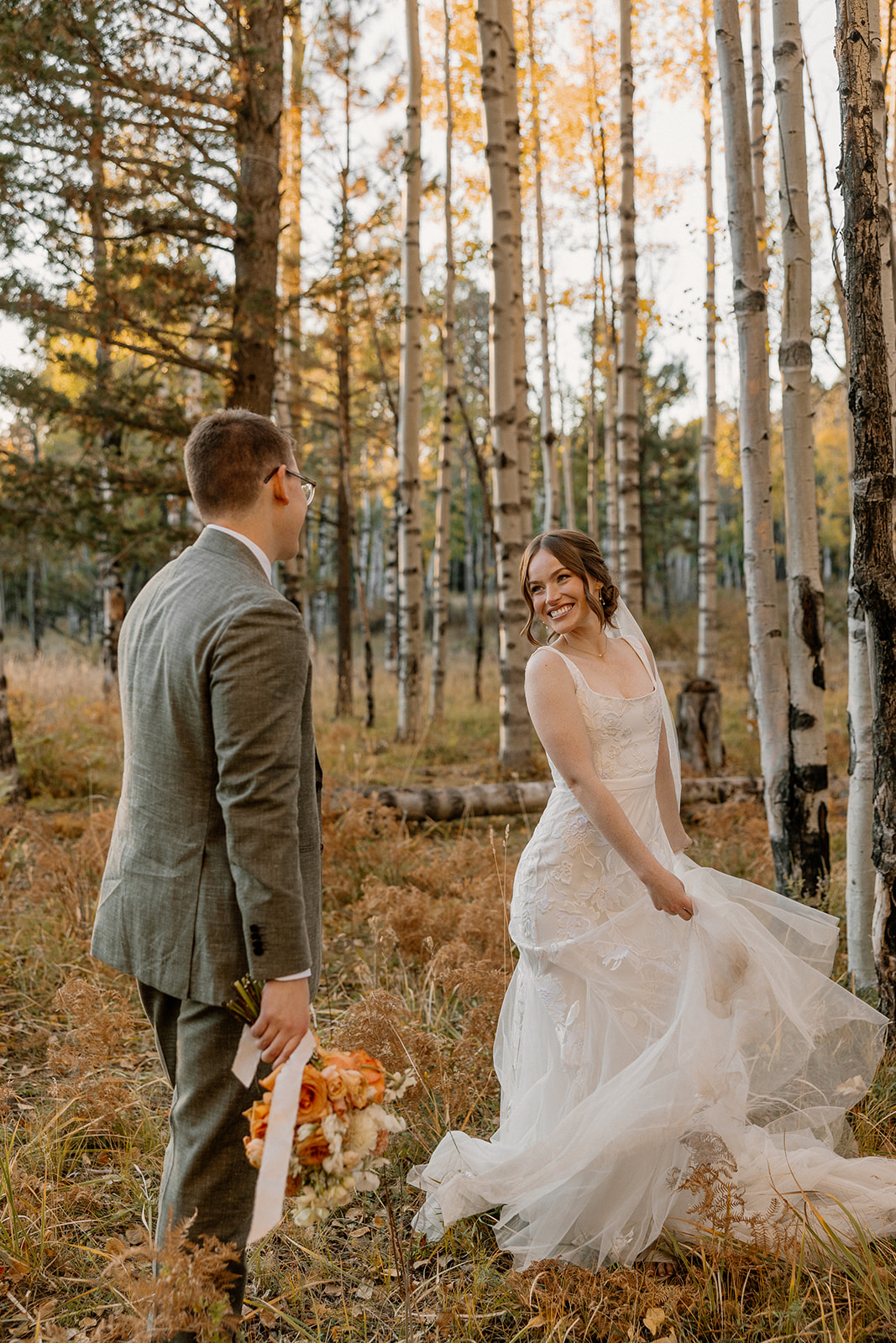 Bride twirls her dress with a playful smile as her groom looks on—warm evening light adds magic to this fall elopement in the aspens.