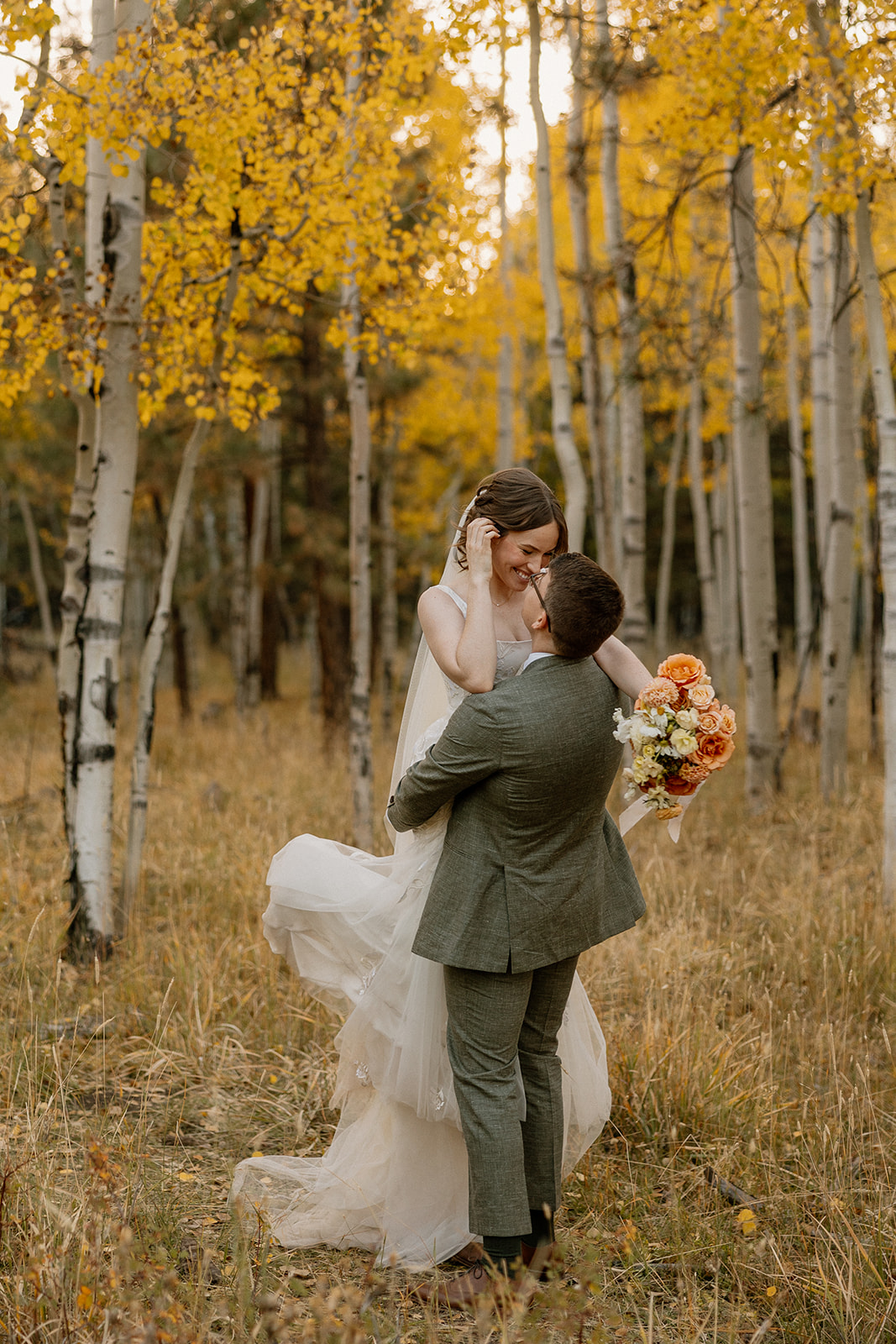 Groom lifting his bride with joy in a golden aspen forest, a candid moment full of love and post-elopement energy.
