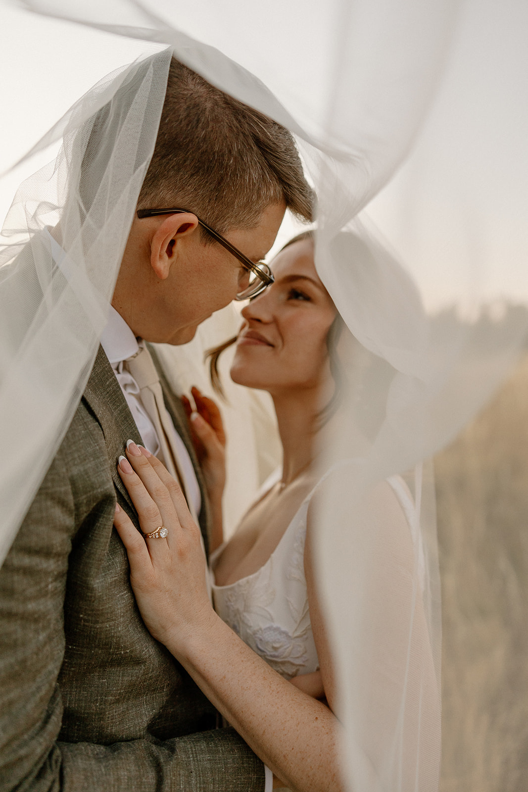 Romantic close-up of bride and groom under a sheer veil, leaning in with soft smiles, symbolizing the quiet intimacy of eloping.
