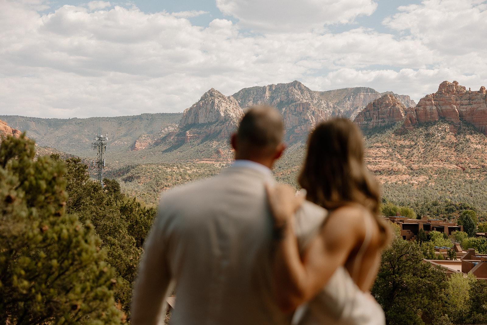 Back view of a couple in wedding attire gazing at the Sedona red rock mountains, representing the emotional moment after deciding how to tell your family you're eloping.
