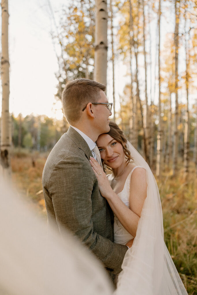 Bride resting her head on her groom’s chest in a glowing aspen grove, one of many grounding moments that follow telling your family you're eloping.
