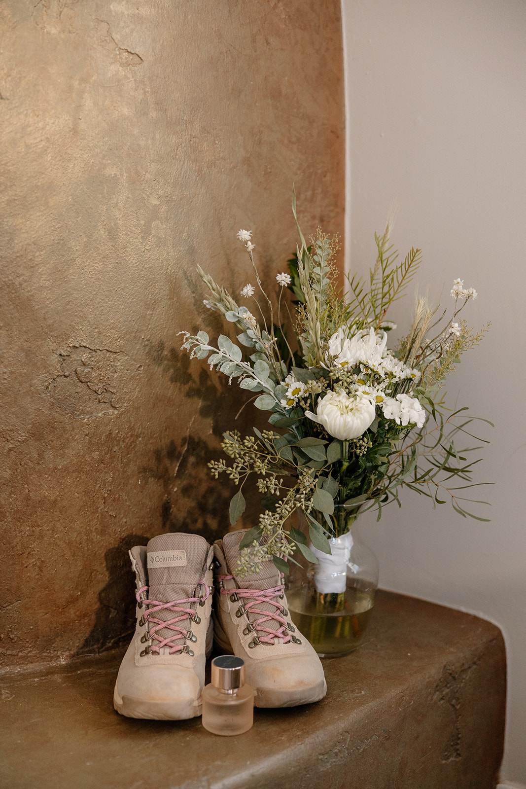 Bridal hiking boots sitting next to a bridal bouquet with white roses and eucalyptus 