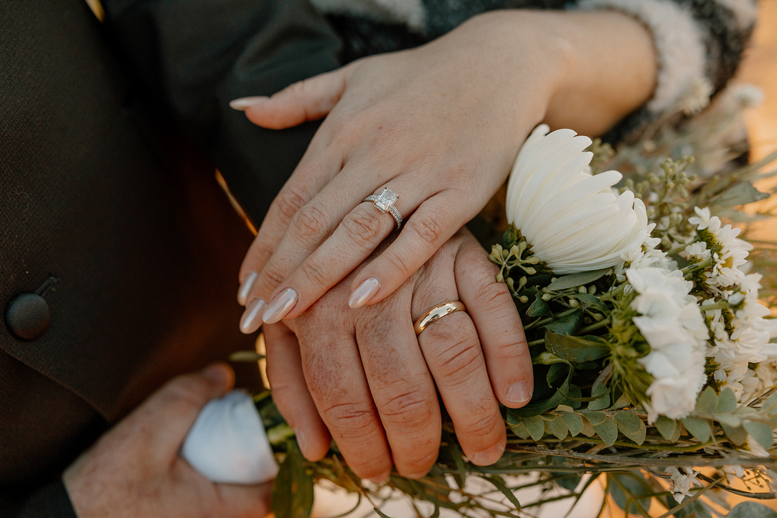 Bride's hand sitting on top of groom's hand showing off wedding rings while holding bridal bouquet
